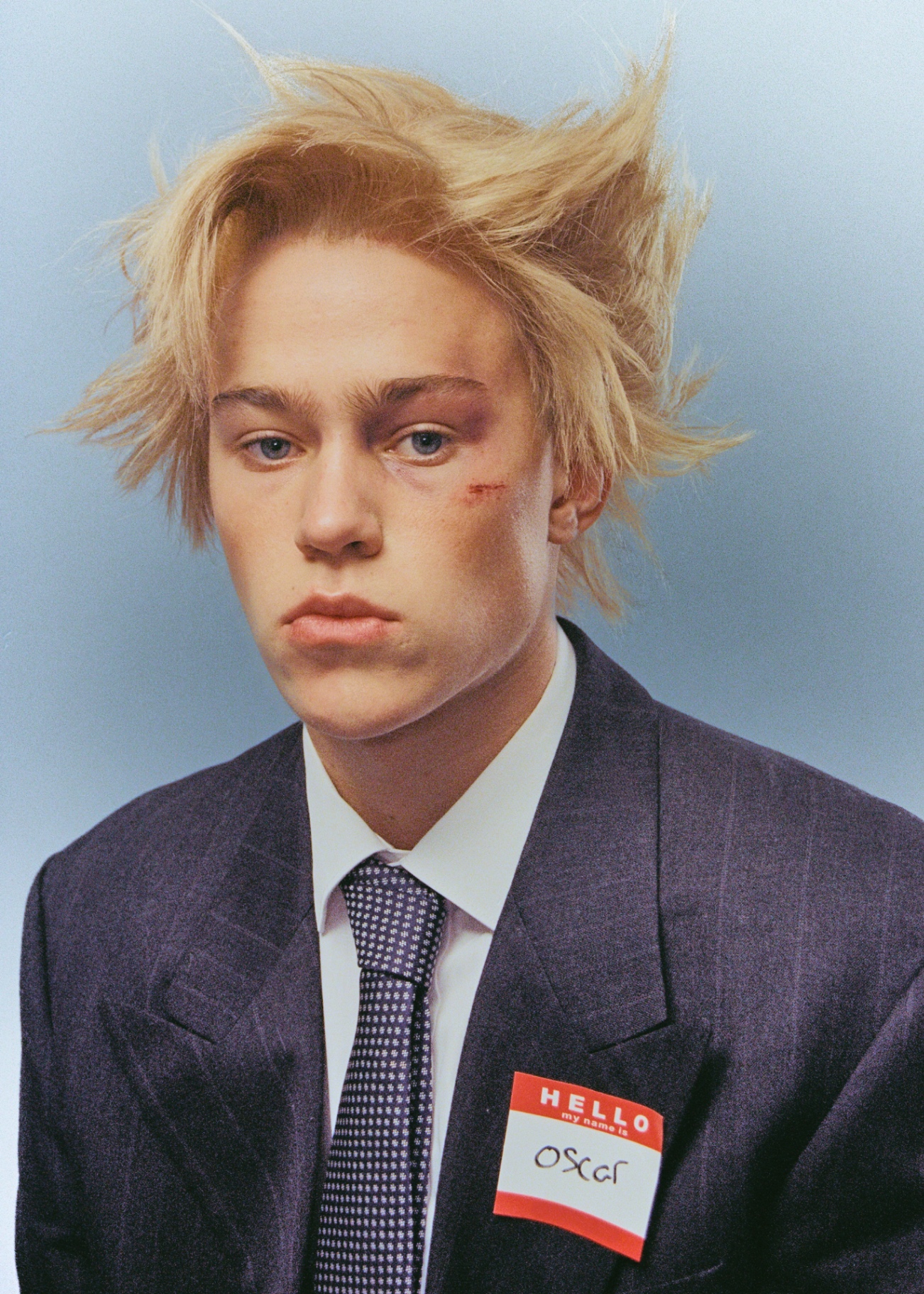 Blond portrait with suit and name tag against blue backdrop